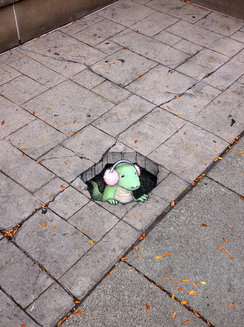 sidewalk chalk drawing of a dinosaur poking his head out of a hole while wearing fuzzy pink earmuffs