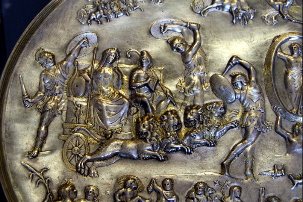 Cybele and Attis (seated right, with Phrygian cap and shepherd's crook) in a chariot drawn by four lions, surrounded by dancing Corybantes (detail from the Parabiago plate; embossed silver, c. 200–400 CE, found in Milan