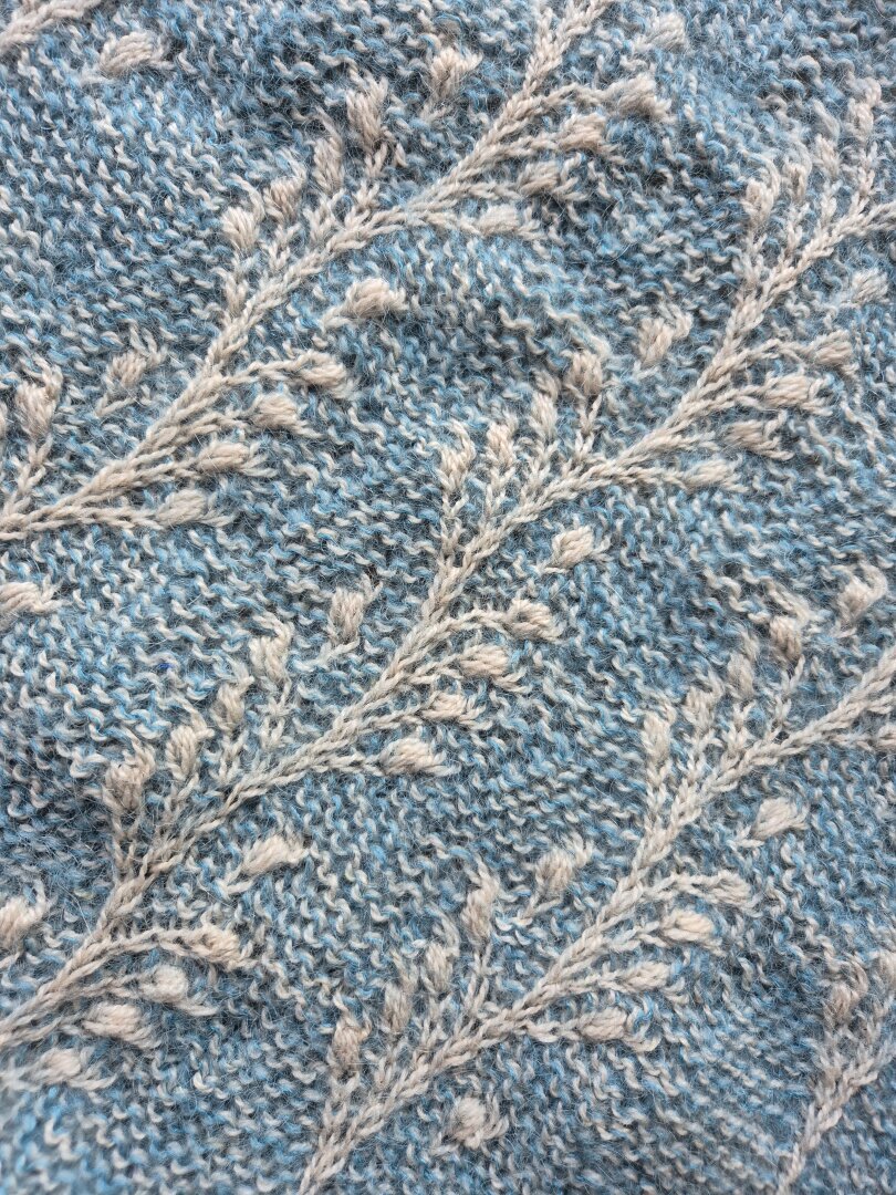 ein Ausschnitt aus einem Strickstück, zweifarbig. Auf einem blauen Untergrund tankt sich ein Muster in Naturweiss