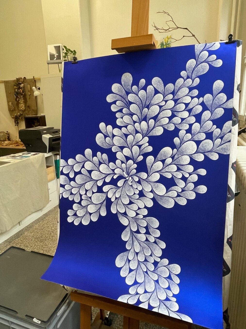 Grande feuille bleue avec dessin pointilliste blanc formé de gouttes blanches bruissantes comme un feuillage. Artwork de Ludivine Cornaglia daté de 2019. Photo prise dans l’atelier de l’artiste, à Nyon, en Suisse.