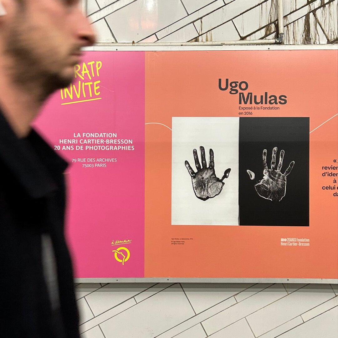 Grande fresque présentant des photographies et citation de photographes, sur fond orange. La fresque se situe sur le quai du métro Hôtel de Ville à Paris