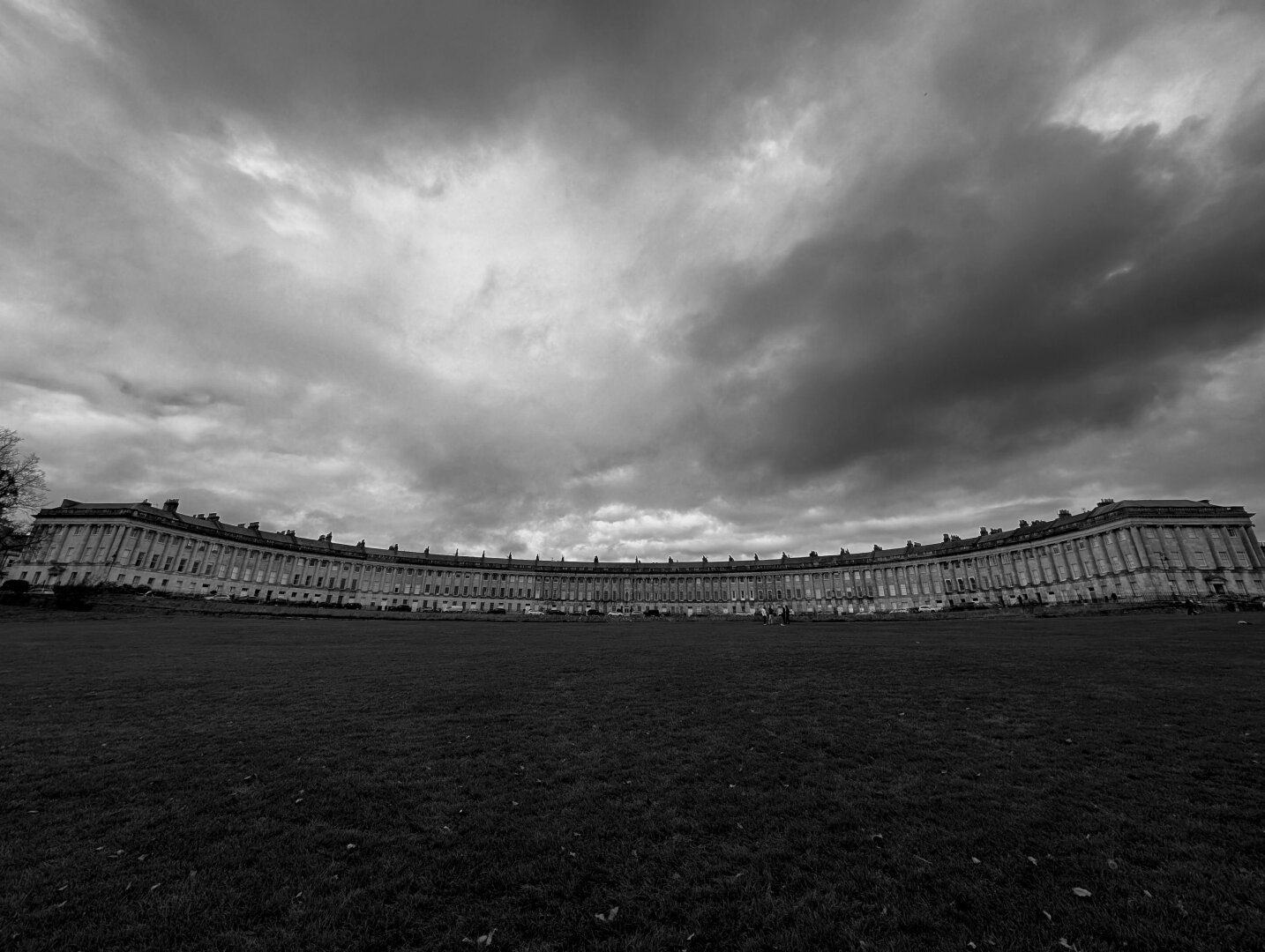 A wide picture of the full royal Crescent in Bath, UK. It's been turned black and white, and the sky has been made to look ominous