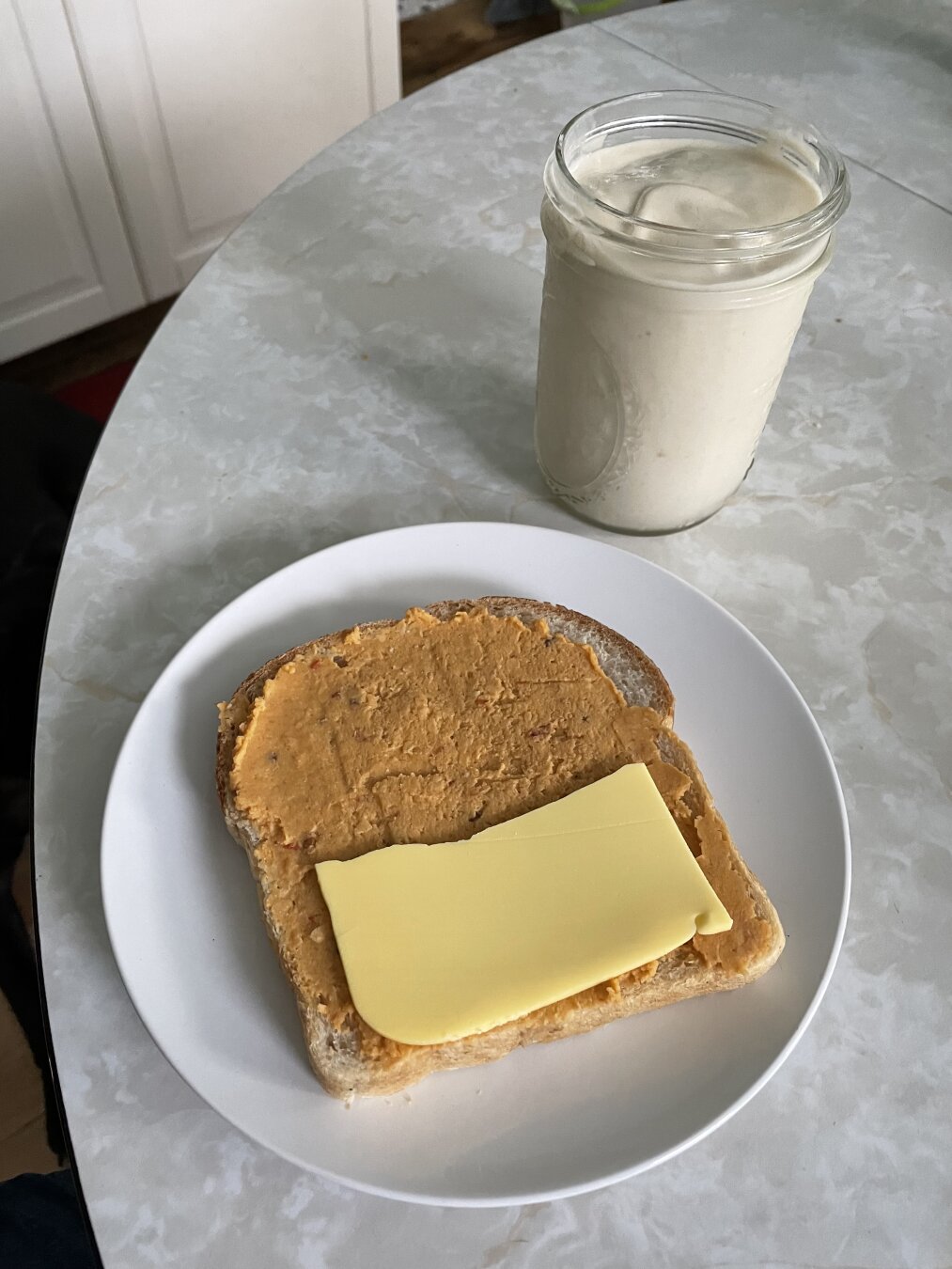 Piece of bread with hummus and cheese on a plate, next to mango smoothie.