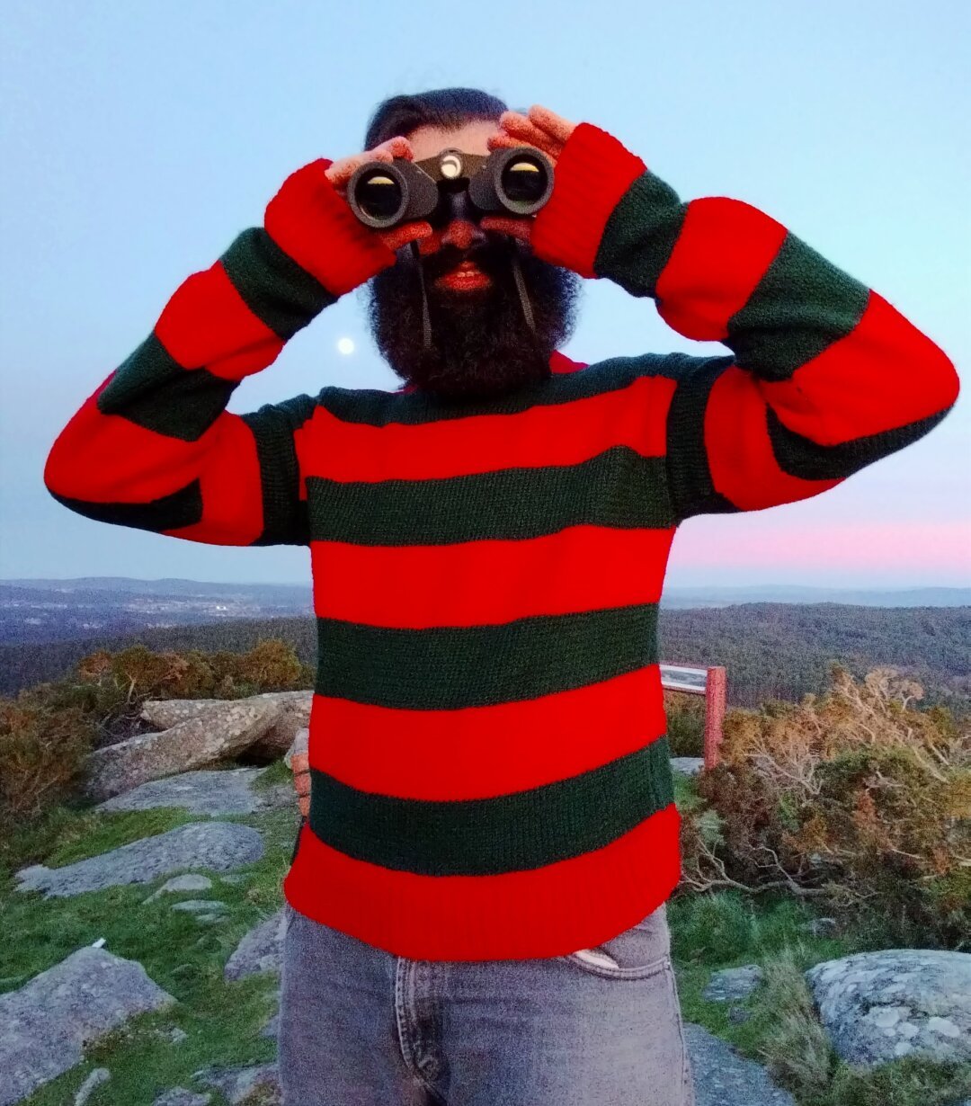 Fotografía do meu mozo no cumio do Monte da Grela ao solpor, mirando por uns prismáticos. Leva posto un xersei que lle fixen semellante ao que leva Freddy Krueger, vermello con raias verdes escuras.