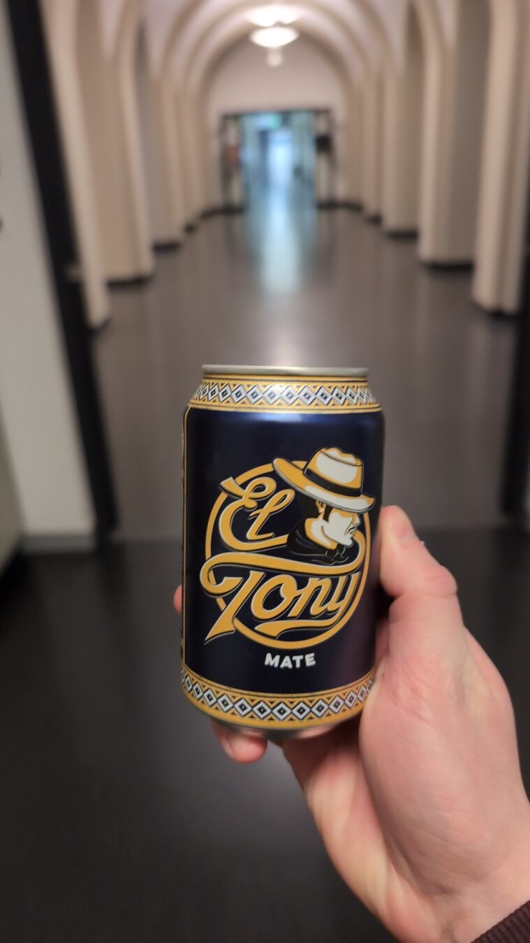 A can of "El Tony" Mate held up by a hand in a hallway