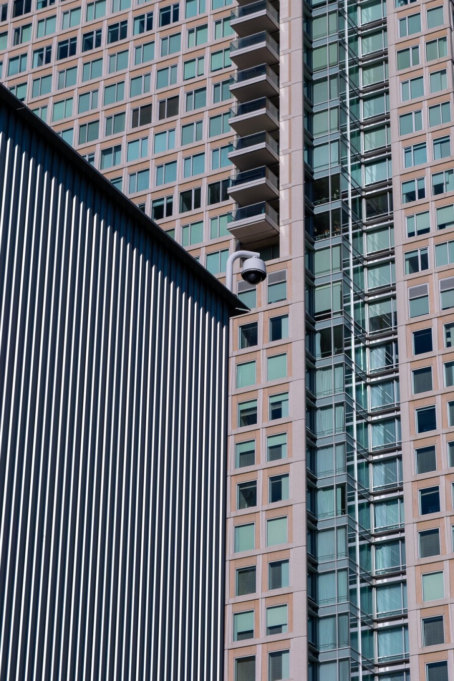 Photo of the exterior of two buildings in downtown San Francisco. The lower-left quadrant of the frame is taken by the Yerba Buena Center for the Arts, with it's periodicly-protruding outer wall givng stark, vertical black and white lines from the shadows and light from off the building. Behind it, the St. Regis hotel, we can see turquoise-aqua windows, almost in the same grid formed by the vertical lines of the Center for the Arts, arrayed on the tan and clay colored wall of the hotel.