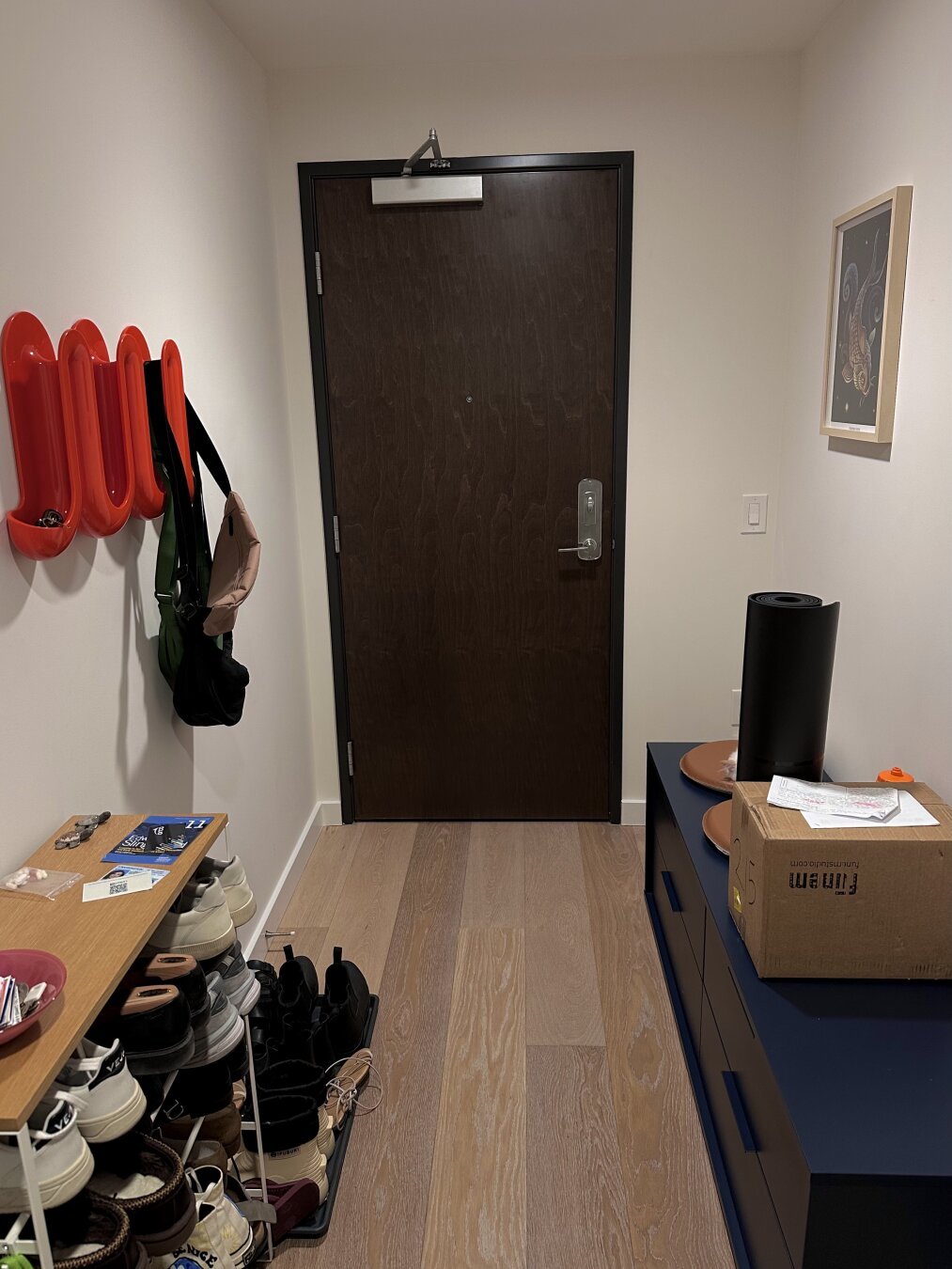 Hallway of apartment entryway. Shoe rack on left, and low blue bench on right. A yoga mat stands on the bench. What's right behind that mat?