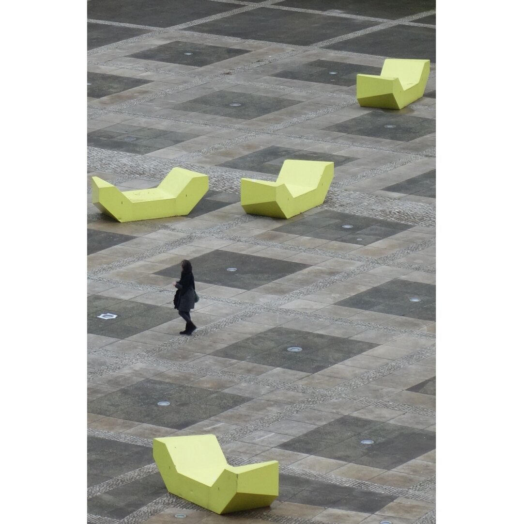 Color picture of a silhouette walking among yellow Plastic banches in the courtyard of Neumunster abbey in Luxembourg