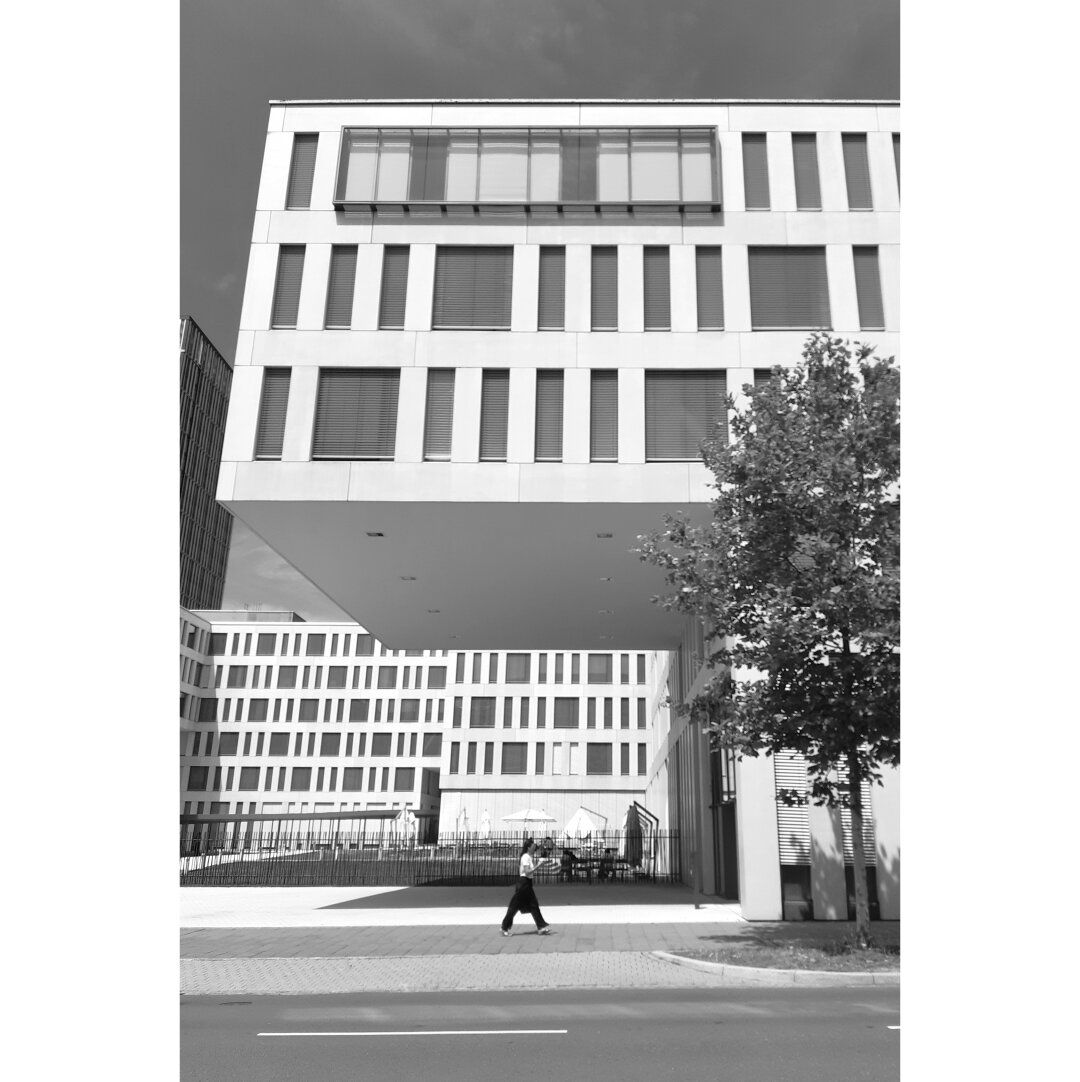 Black and white street photography taken in Luxembourg city showing a pedestrian passing by the EIB buildings on the Kirchberg.