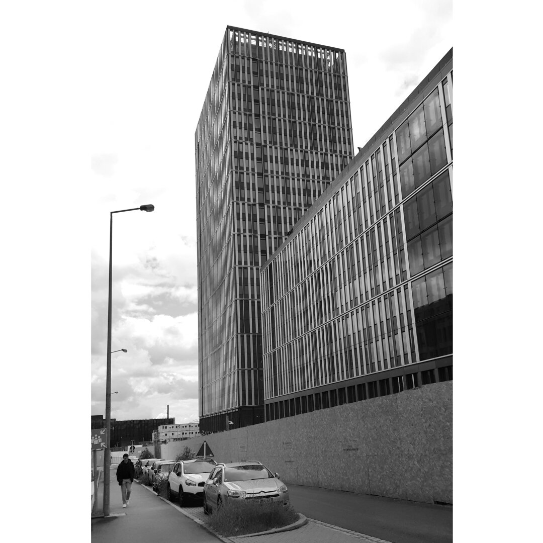 Black and white street photography taken in Luxembourg city showing a man walking in an empty street next to a skyscraper.