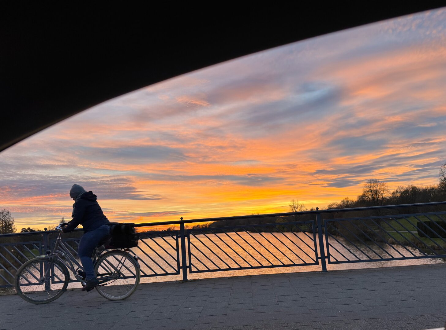 Abendhimmel über dem Aasee, auf der Brücke ein Radfahrer im Gegenlicht, Foto durch ein offenes Autofenster