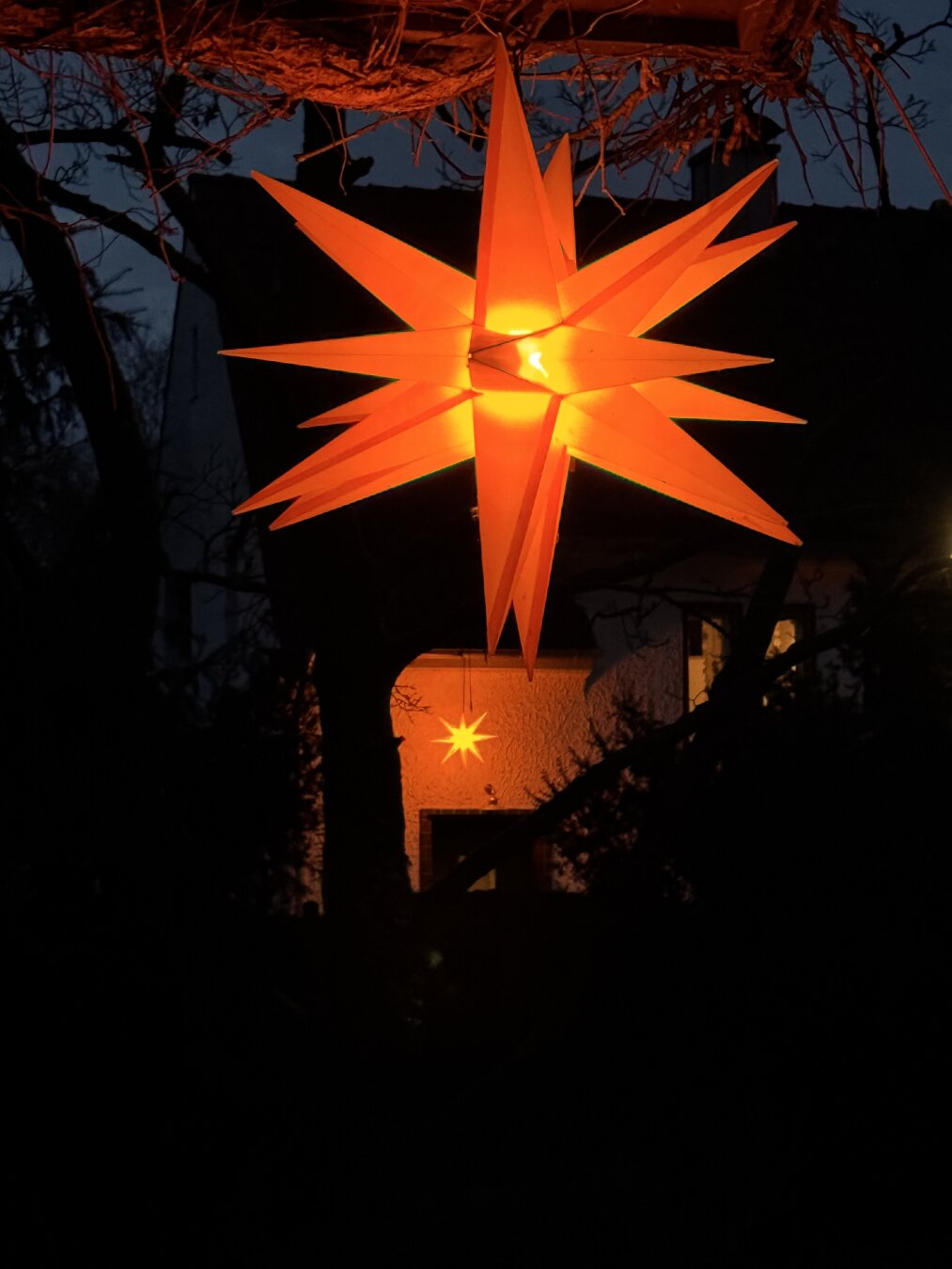 Ein orange leuchtender Stern und weiter im Hintergrund ein weiterer, der an einem Nachbarhaus hängt, irgendwie passend zum zweiten Advent.