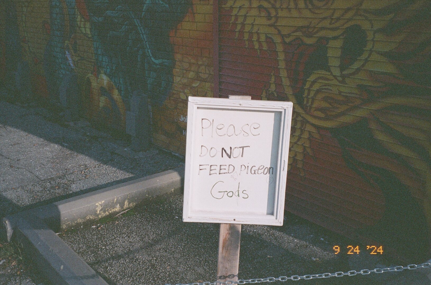 a sign reading 'please do not feed pigeon gods'. pentax espio expired kodak gold 400