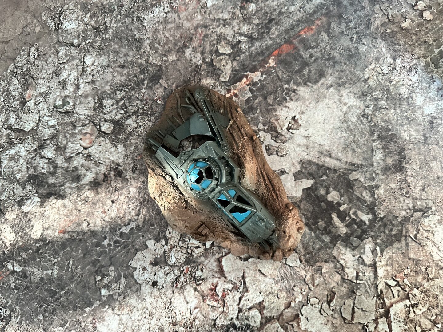 Top down view of a printed miniature wargamjng battle mat, depicting concrete rubble, with an old Warhammer 40K plastic scenery piece in the middle