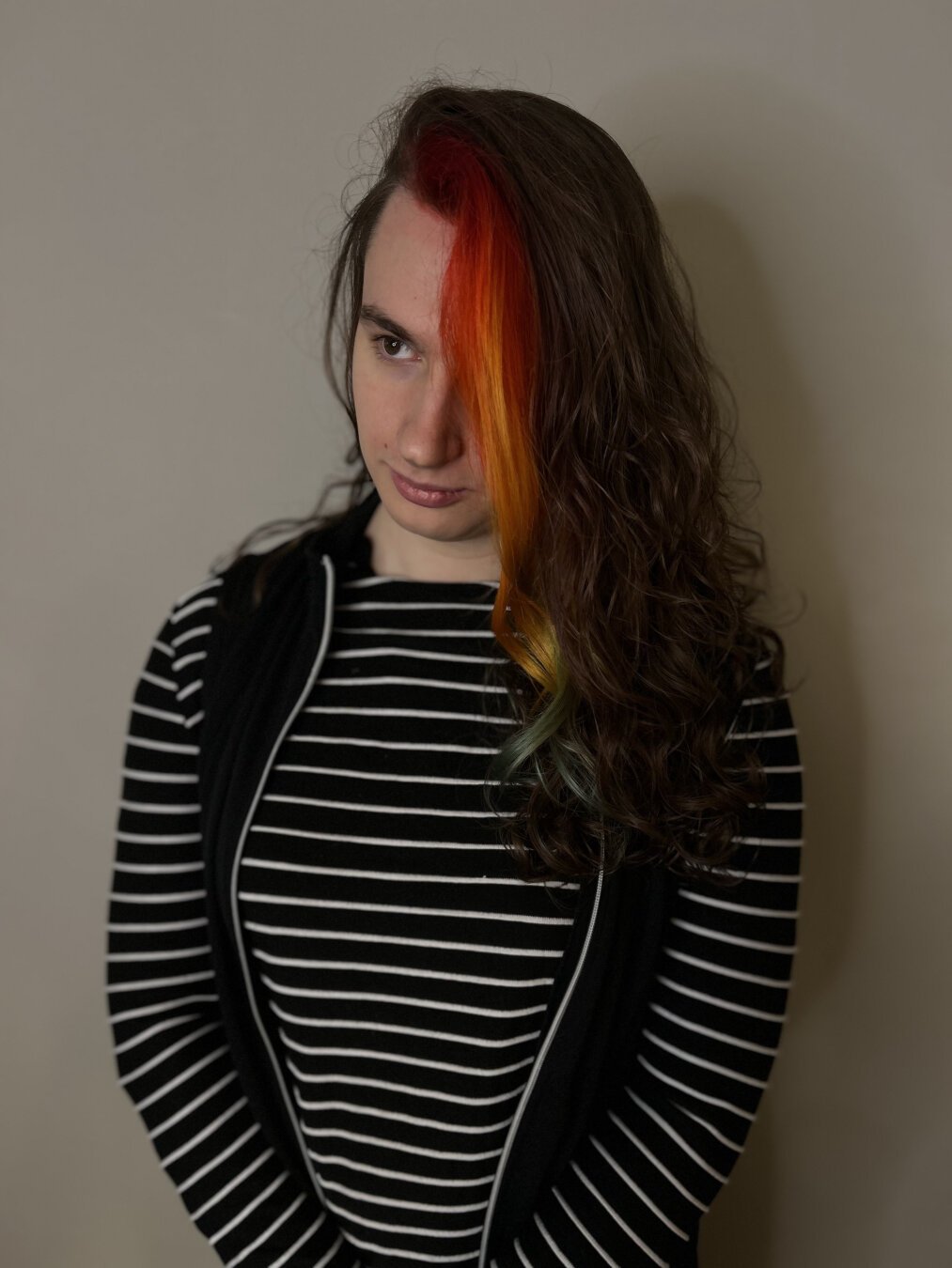 An image of twyn!b with redyed hair - the hair is red at the top, then fades into orange, then yellow, then a greenish blue.