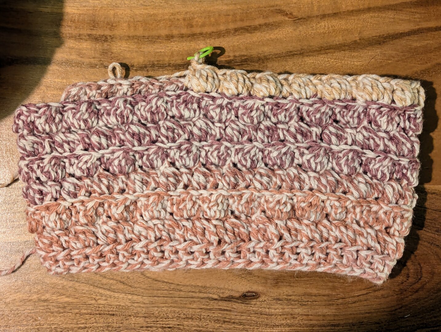 A partially finished crochet cowl made with alternating double crochet and cluster stitches in the back loop only. The yarn cake is two toned with a beige running through the entirety while also going from peach to coral to mauve to an almost orangey pale yellow. The pinky shades look a bit like lipstick colors lol.