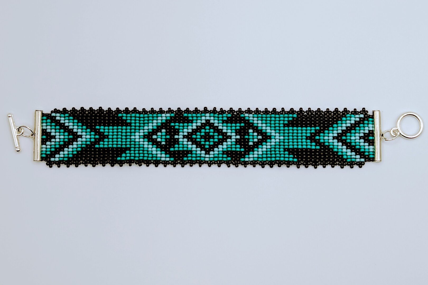 A black and turquoise beaded bracelet made with square stitch (which resembles loom work) and sporting a southwestern design. The bracelet was finished with a silver toggle clasp.