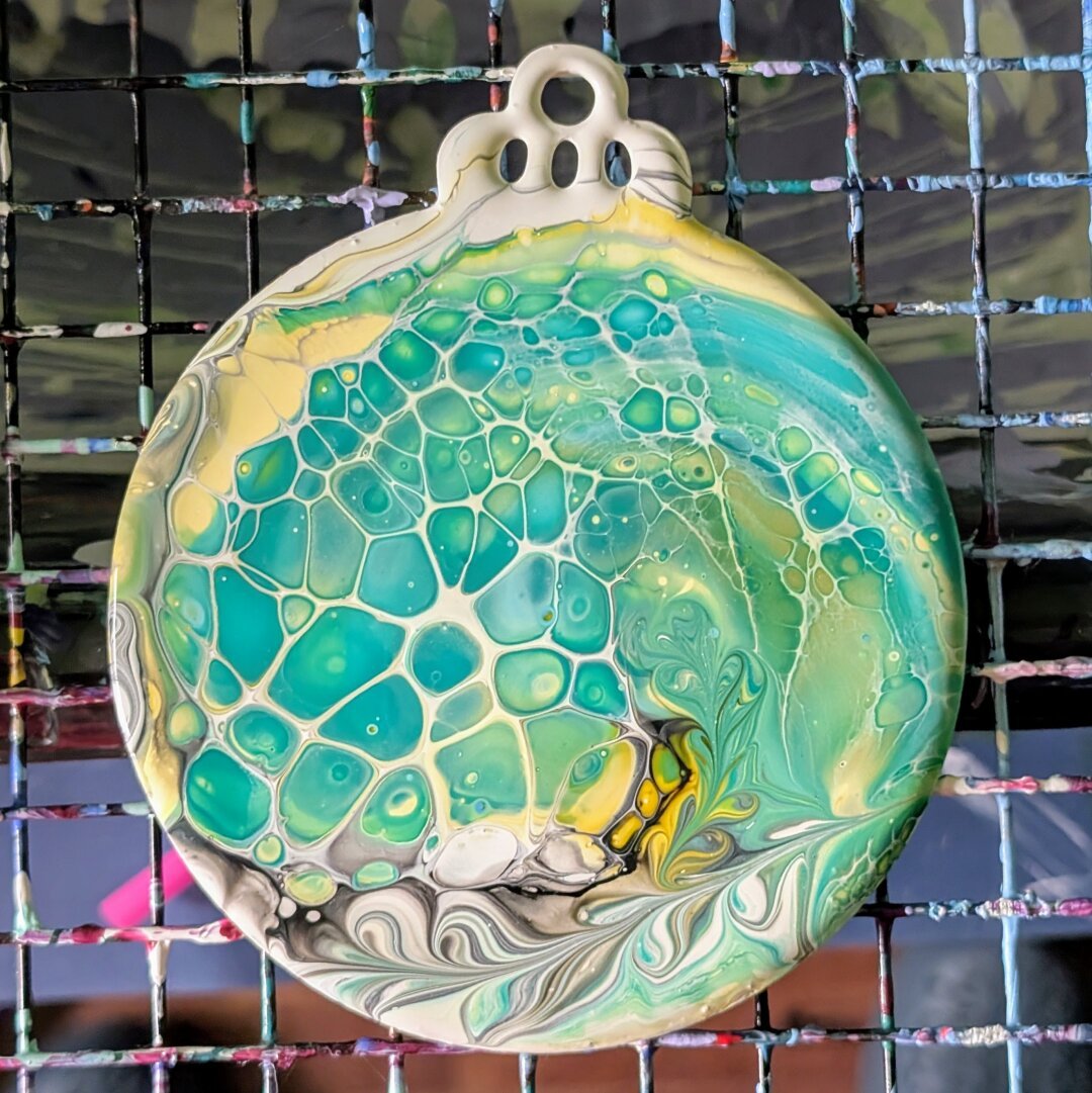 A wrecked Shelee bloom swipe on a flat, round holiday ornament. The color palette is shades of yellow, turquoise, and green with white and black cell activators.