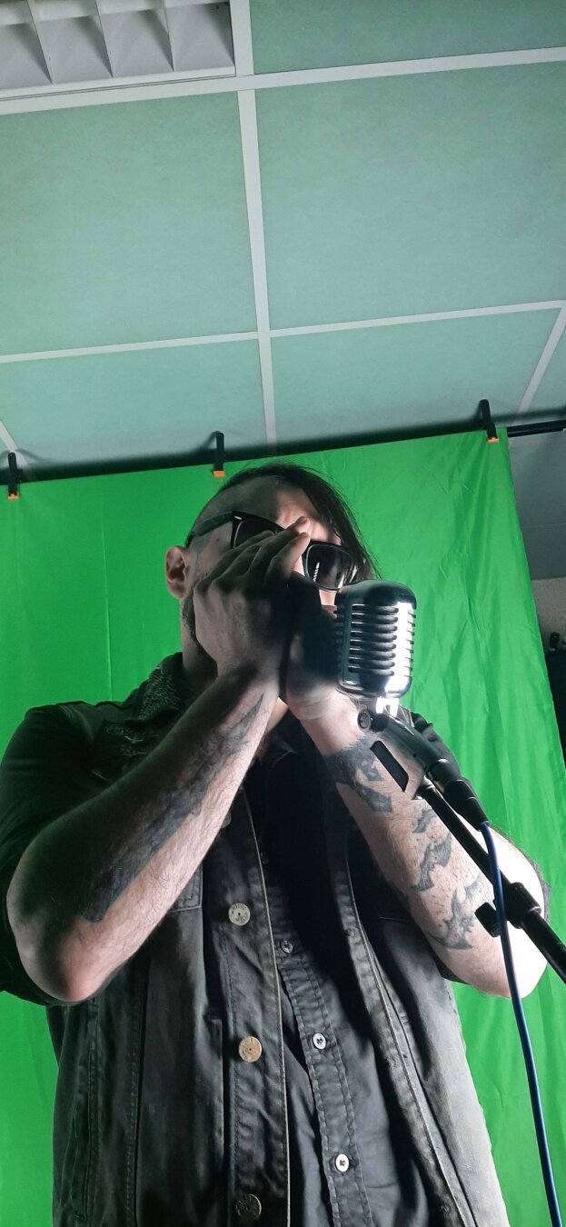 Man with a punk rock style recording harmonica in front of a green screen