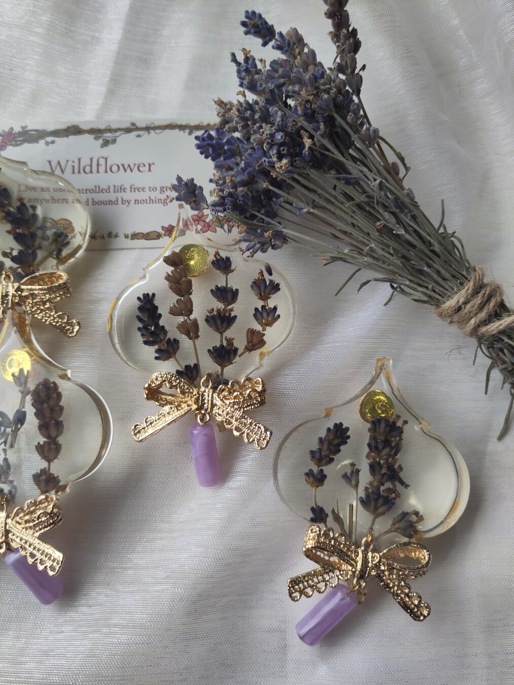 In the picture a garland of lavender on the right and featured is the eternal lavender brooch by MercuRea brand which consists of lavender encased in resin and a golden metallic bow