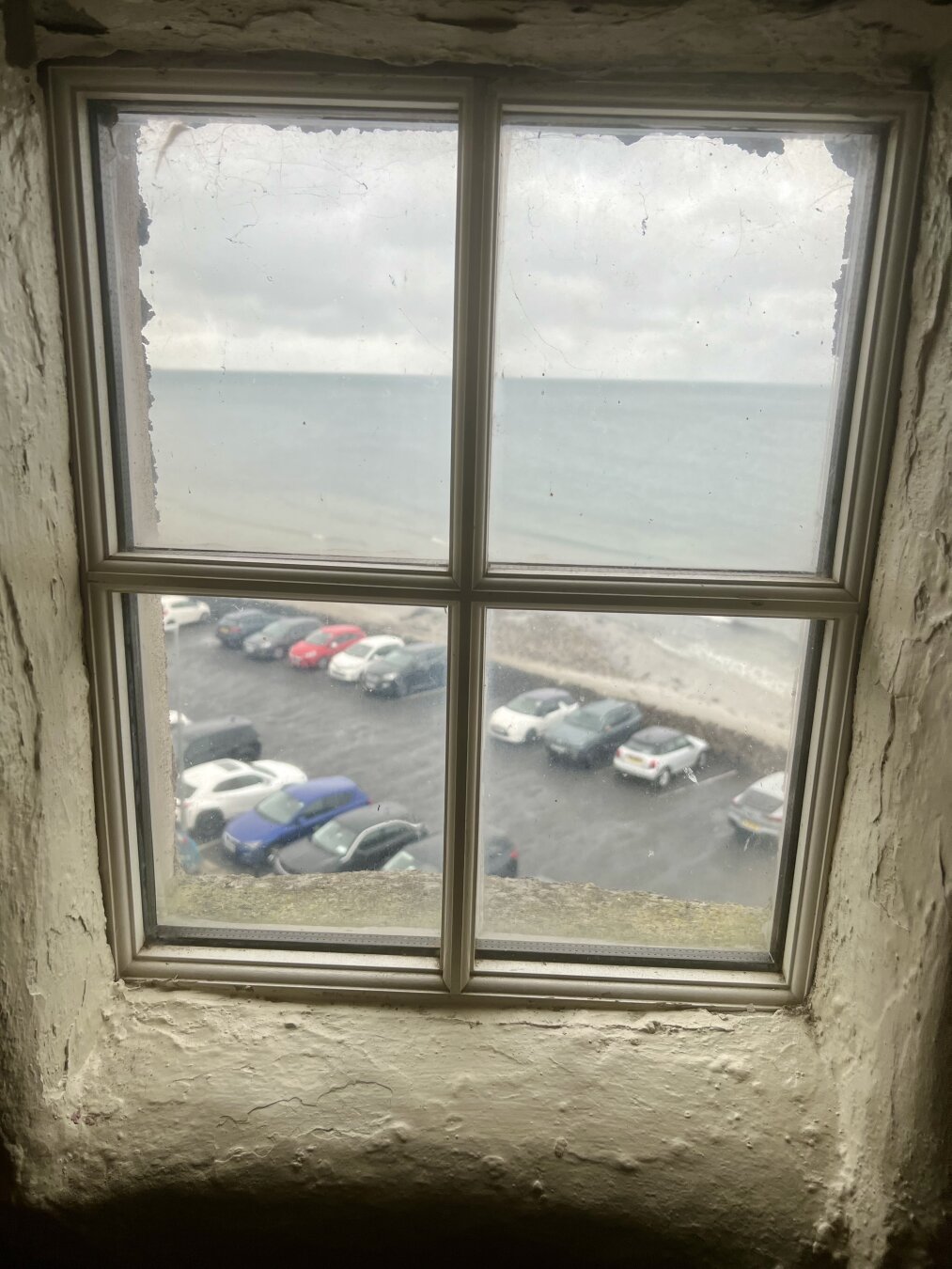 An old looking window looking out onto the seafront and car park