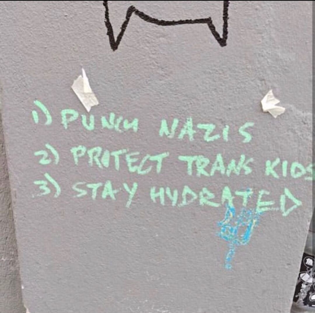 Graffiti on a wall saying "1. Punch nazis. 2. Protect trans kids. 3. Stay hydrated."