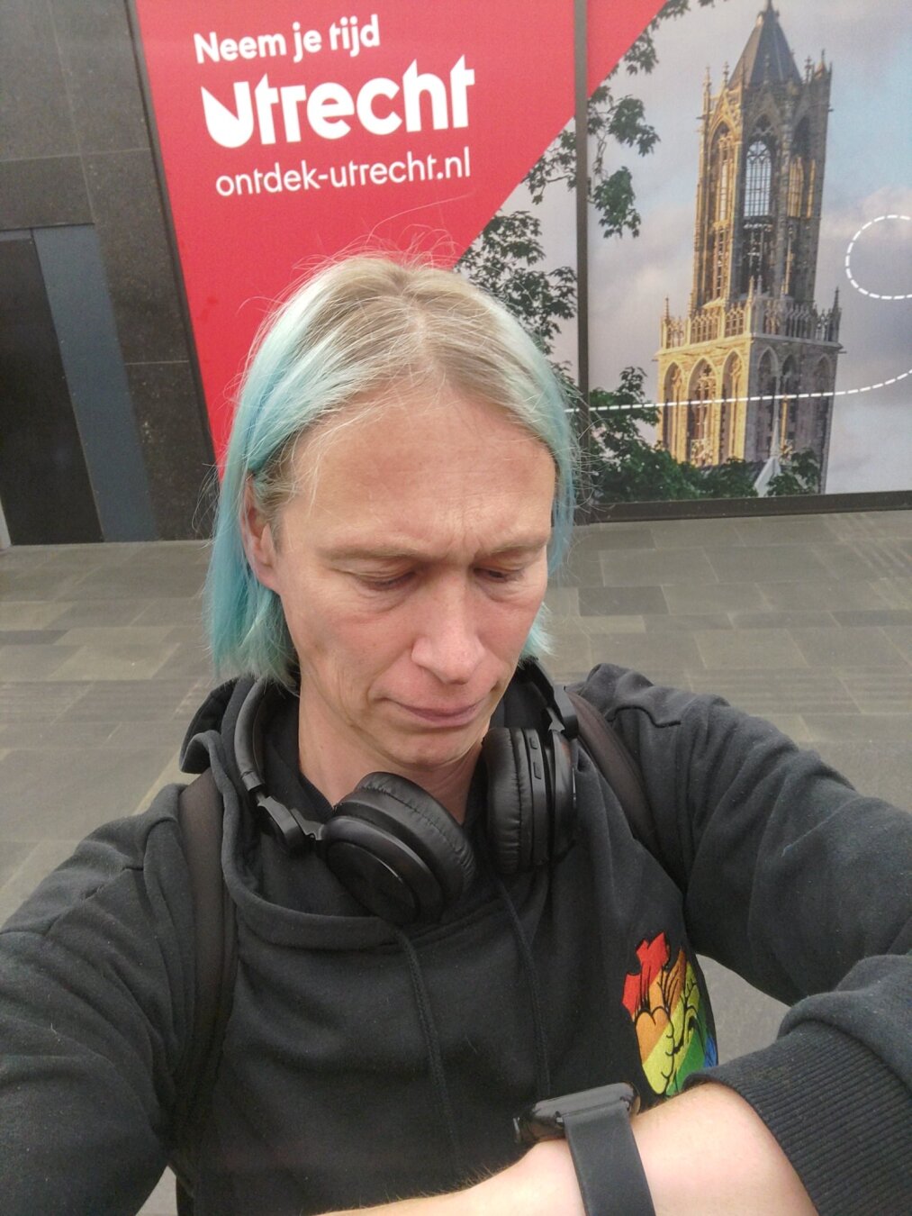 Background: empty shop covered by sticker advert for the municipality of Utrecht carrying the text 'neem de tijd' (Dutch for 'take your time'). Foreground: me impatiently looking at my watch