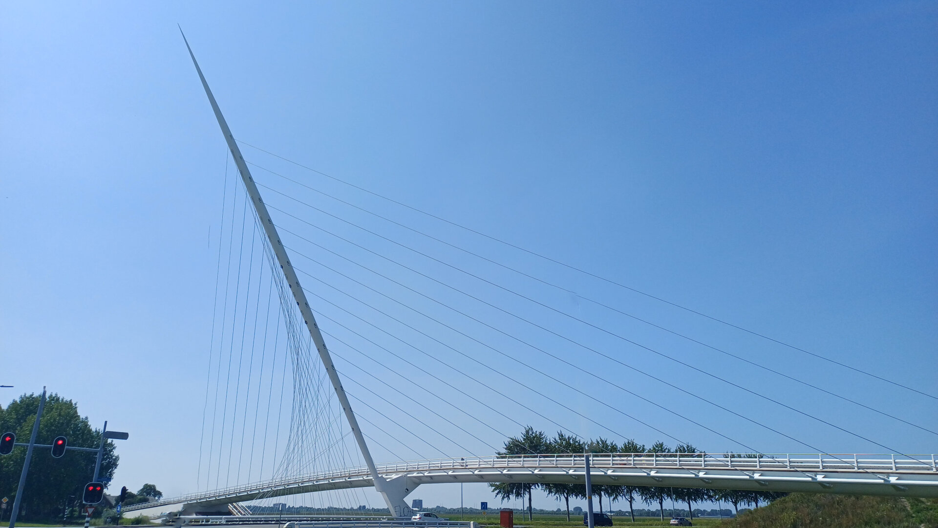 Asymmetrical slender suspension bridge from the side against a clear blue sky. The pillar is leaning to the side
