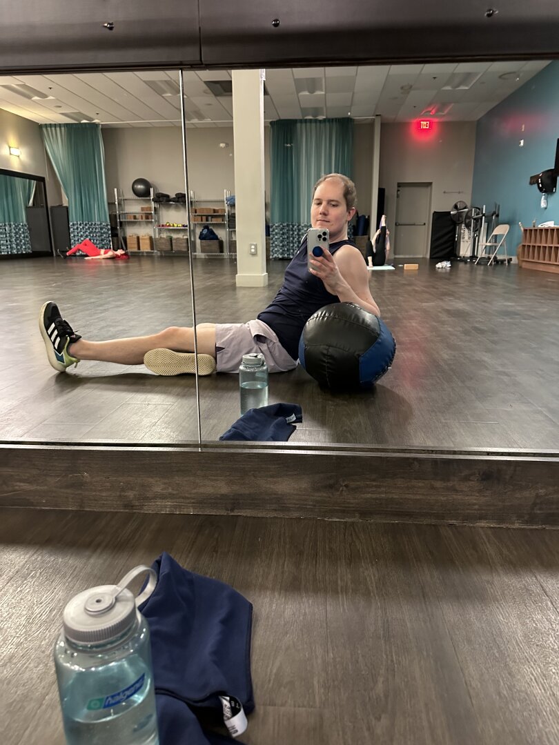 Me on the floor stretching my quads and reclining on a medicine ball.