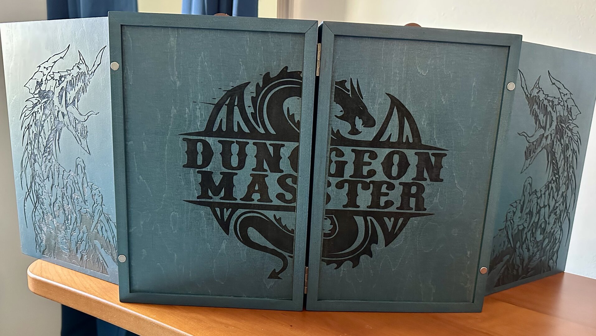 The front of a blue wooden DM screen with dragons and the words DUNGEON MASTER engraved on the panels.