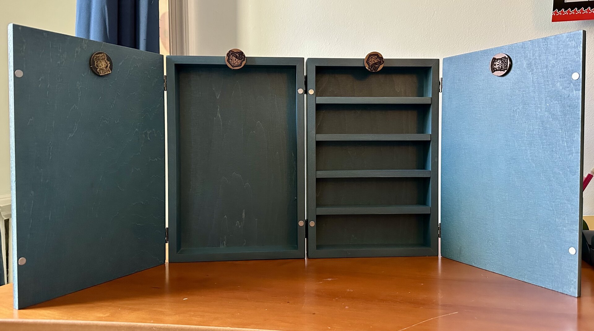 The back of a blue wooden DM screen with magnetic clips and built in shelves.