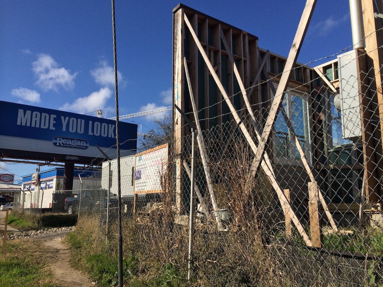 Title: Reagan Made You Look the Other Way

Alt Text: Photograph of a construction site with a billboard in the background. The billboard, advertising Reagan, says 