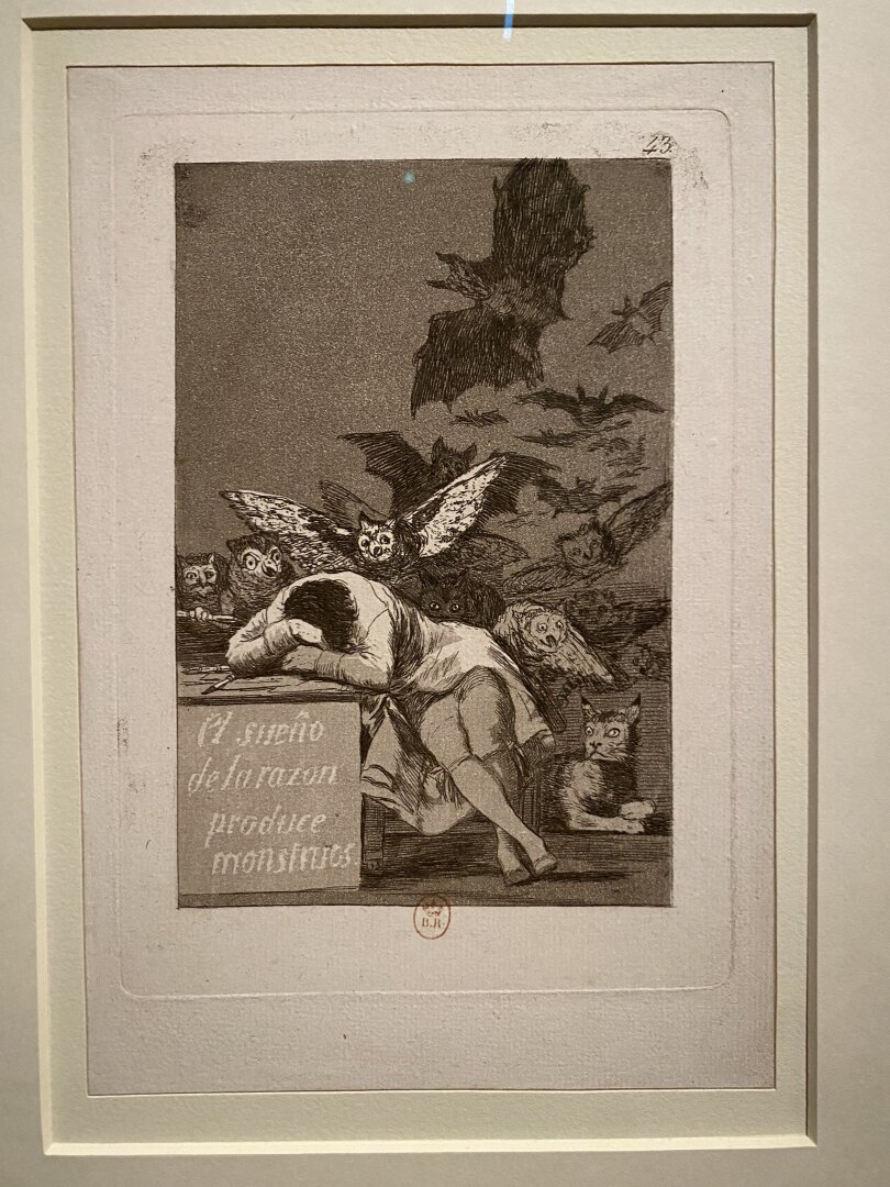 Black and white engraving on paper by Goya depicting a sleeping man with owls and bats invading the space. “El sueño de la razón produce monstruos” can be read