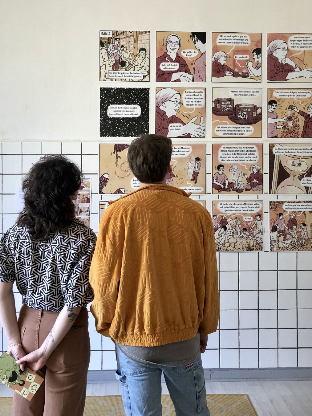 Zwei Menschen stehen vor der gekachelten Wand im Atelier und schauen sich die großformatigen Panels meines Comics ‘Rania’ (aus der Anthologie ‘Wie geht es dir?’, Avant, 2025) an.

Der Comic erzählt von einem Gespräch mit der Bremerin Rania Enan und der Frage, wie wir als Gesellschaft zusammenfinden können in Zeiten extremer Polarisierung und Vereinzelung.