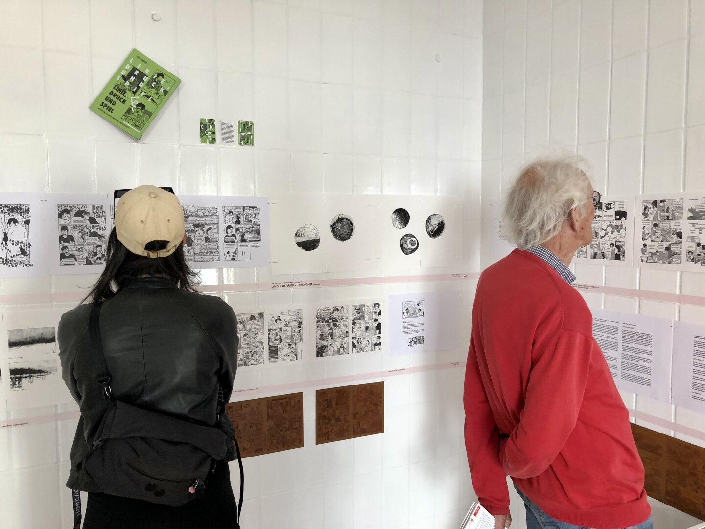 Menschen stehen vor einer weißen Wand und schauen sich eine Ausstellung an. An der Wand hängen die einzelnen Druckbögen aus meinem Künstlerbuch ‘Linie, Druck und Spiel’ (Kulturhuef-Residenz, 2024).

Das Buch ist eine Art fragmentierter Bericht zu meiner Residenz im Druck- und Spielkartenmuseum Kulturhuef in Grevenmacher, Luxemburg, mit Gastbeiträgen von Judith Lena Bartels und Misch Valente. Es wurde mit verschiedenen Drucktechniken (Siebdruck, Risografie, Offsetdruck, Buchdruck Heidelberger Tiegel, Radierung, Monotypie) realisiert.

Unter den Druckbögen kleben ein paar der orangen Nylonprintplatten, die für den Druck mit dem Original Heidelberger Tiegel verwendet wurden.