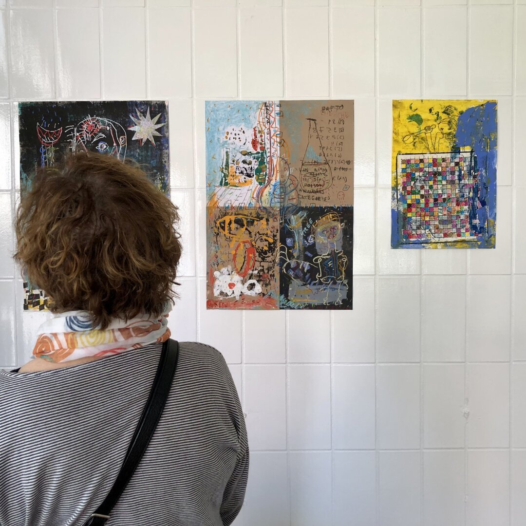 Ein Mensch steht vor einer gekachelten, weißen Wand und schaut sich die Arbeiten meines Gasts, dem Künstler Misch Valente aus Wormeldingen/Lux., an.

Es sind Arbeiten in einer Mischtechnik aus Monotypie, Kreidezeichnung und abstrakter Malerei.