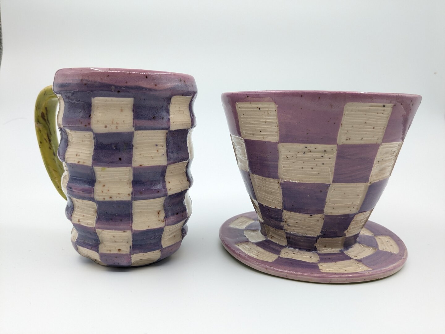 Handmade purple checkered mug with green handle and handmade purple checkered coffee dripper sitting next to each other