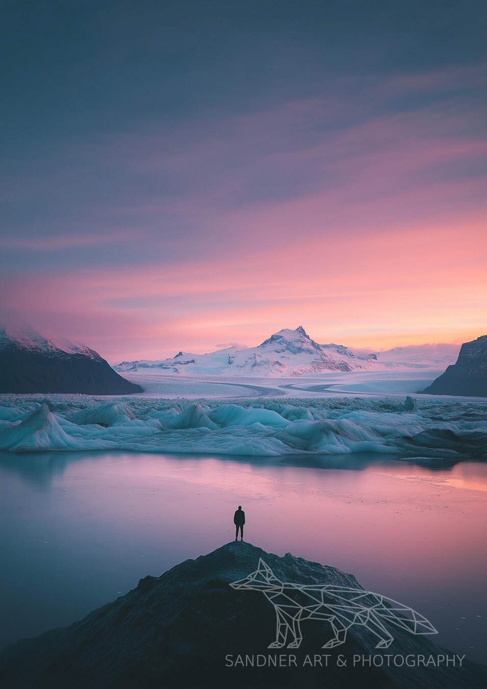 A solitary figure stands on a rocky outcrop, gazing over a glacial lagoon with floating icebergs, framed by a sweeping glacier and towering snow-capped mountains. The sky is painted in soft pastel hues of pink, purple, and blue, casting a tranquil glow over the icy landscape. The image evokes a sense of solitude and awe in the face of nature’s vast beauty.