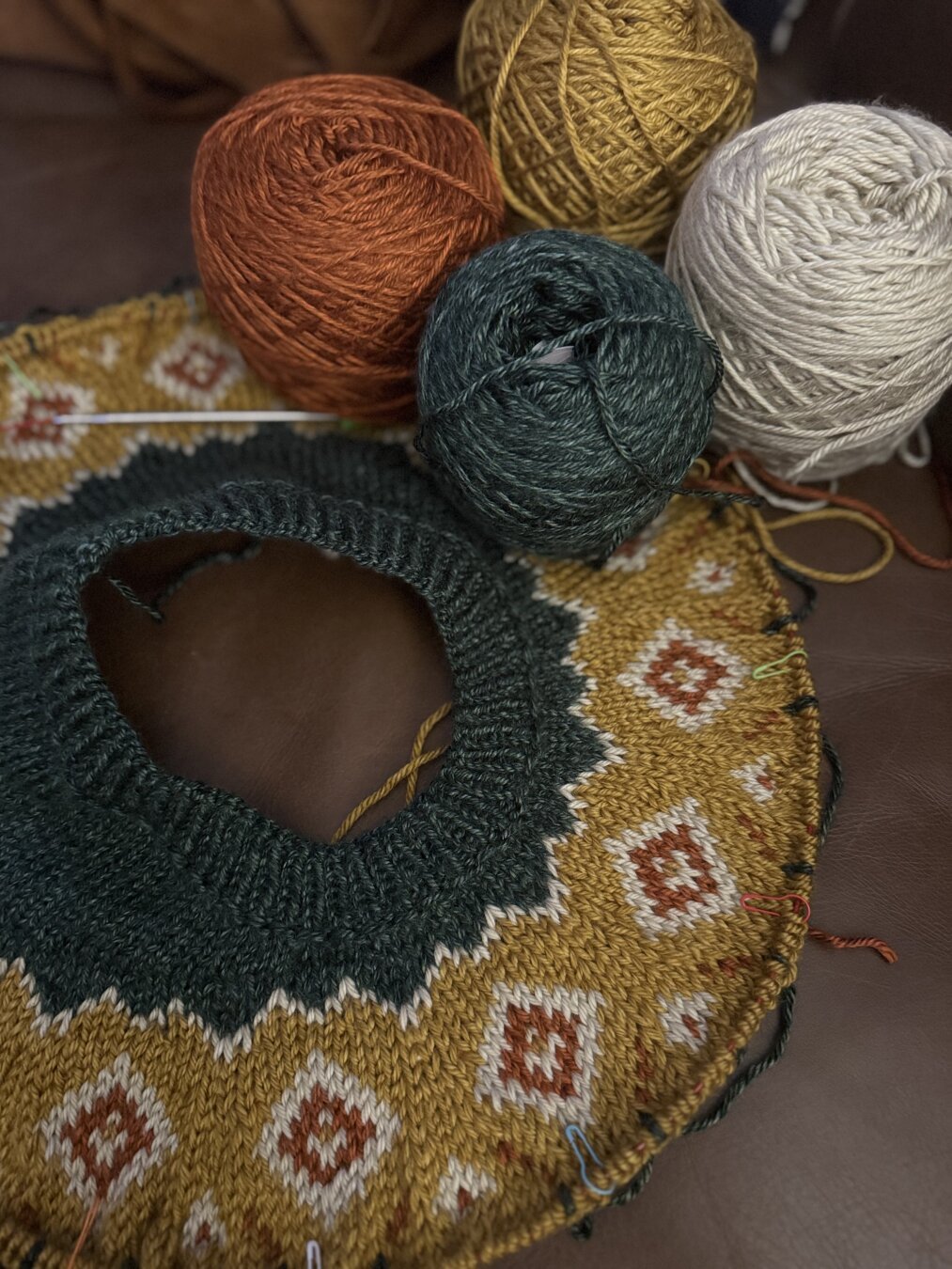 A knitted sweater yoke with several yarn cakes in white, yellow, green, and rust.