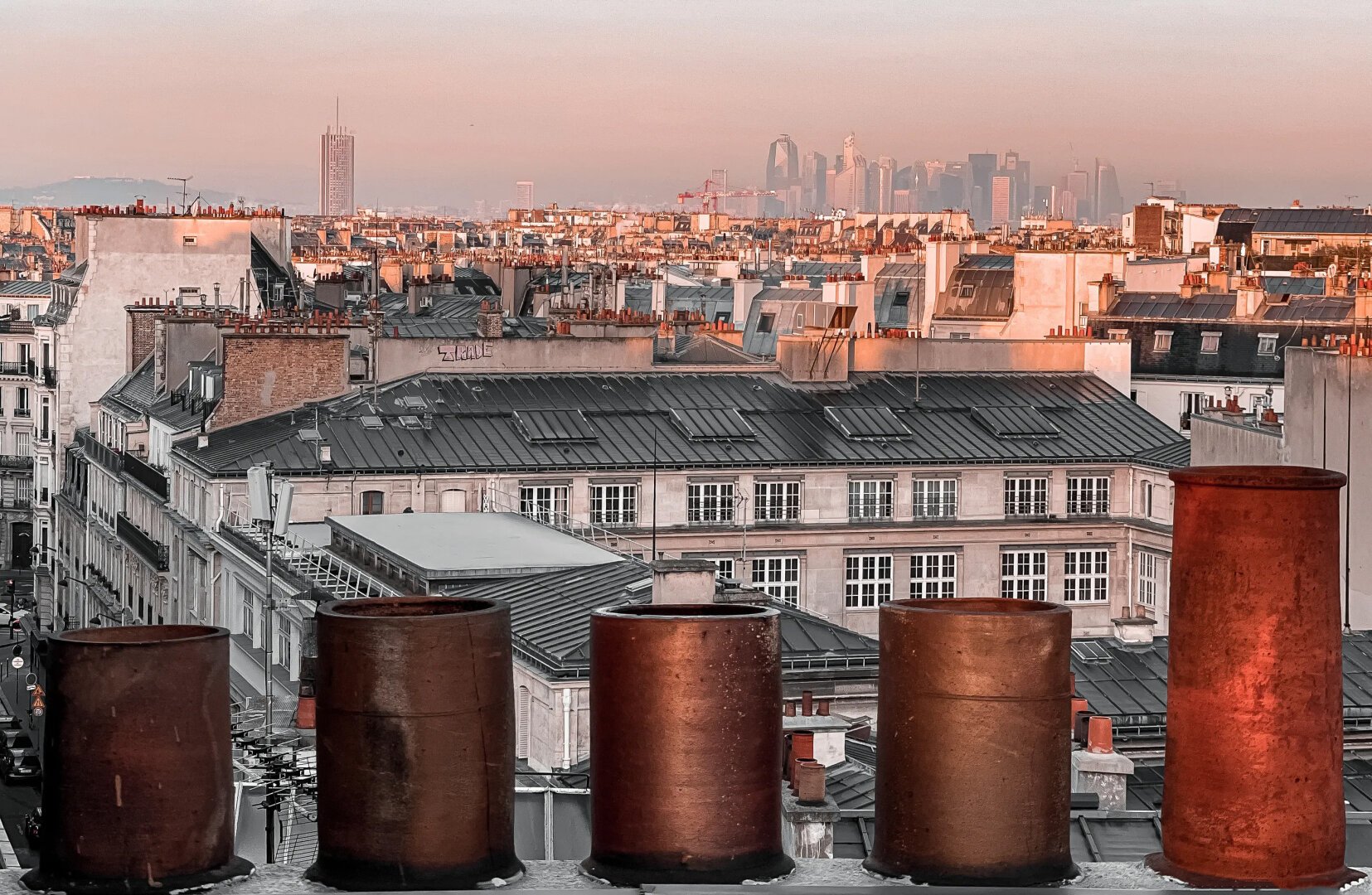 5 cheminées depuis une toiture. La plus grande se trouve à droite. On a l'impression que ce sont 5 personnes qui regardent les toits de Paris en arrière-plan.