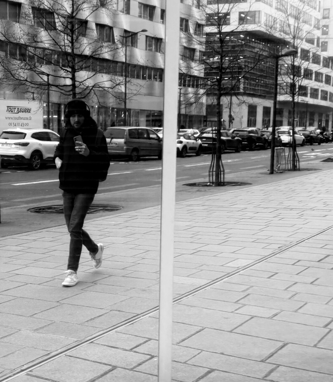 Un homme avec un téléphone dans la main. Il porte un bonnet. La photo est en noir et blanc.