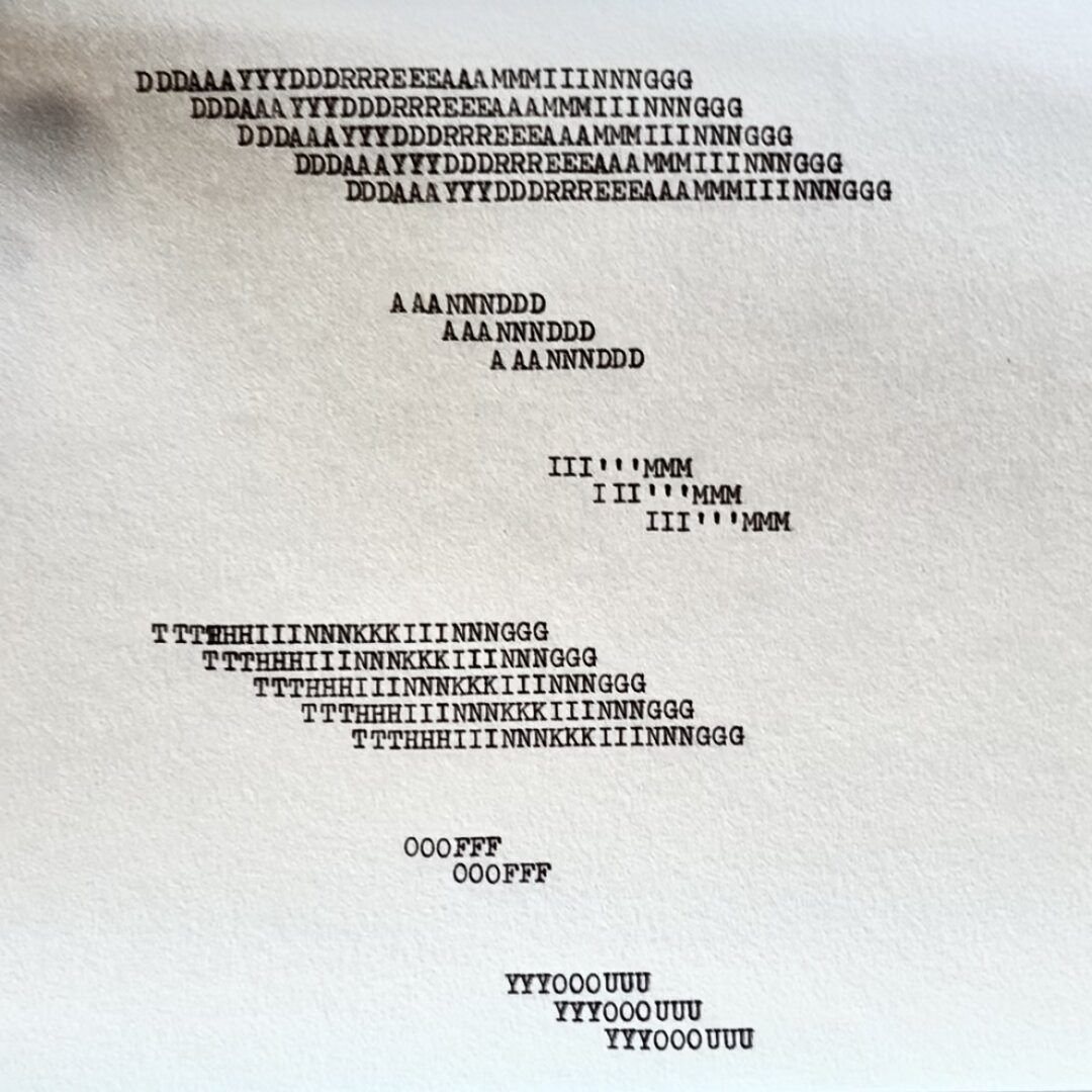 A picture of a concrete poem typed on a white paper with a black ink ribbon; ‘daydreaming and i’m thinking of you’. The letters and words are repeated and travel down the page, creating 6 rectangles. 2 big ones for the longer words ‘daydreaming’ and ‘thinking’, and 4 smaller once for the rest of the words.