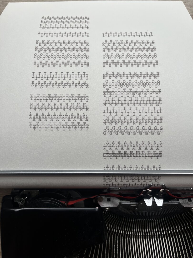 A photograph of a paper that is rolled within a typewriter portraying a concrete poem. A row of black letters repeats, making the message as thick as a brick, stating “All I know is that I know nothing at all”