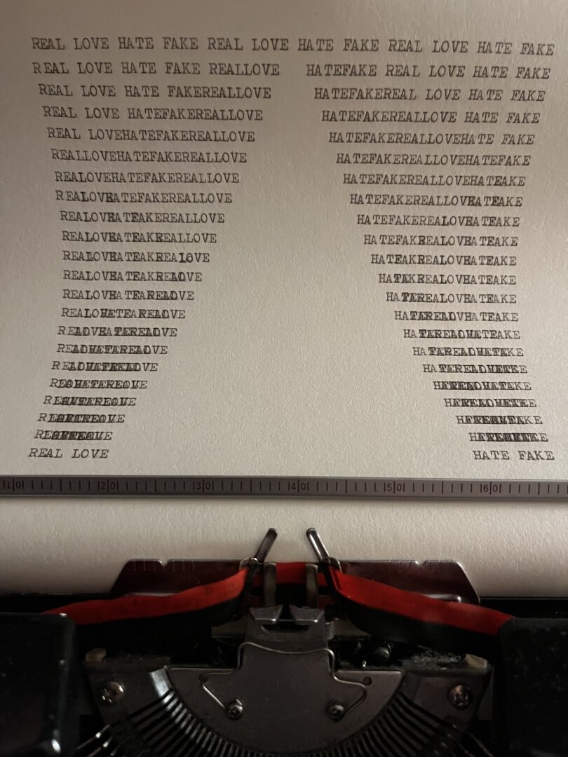 An image of an paper with the words love, hate, real and fake; sitting in the typewriter as it has just been created. By artist Sebastián Andrés Vis