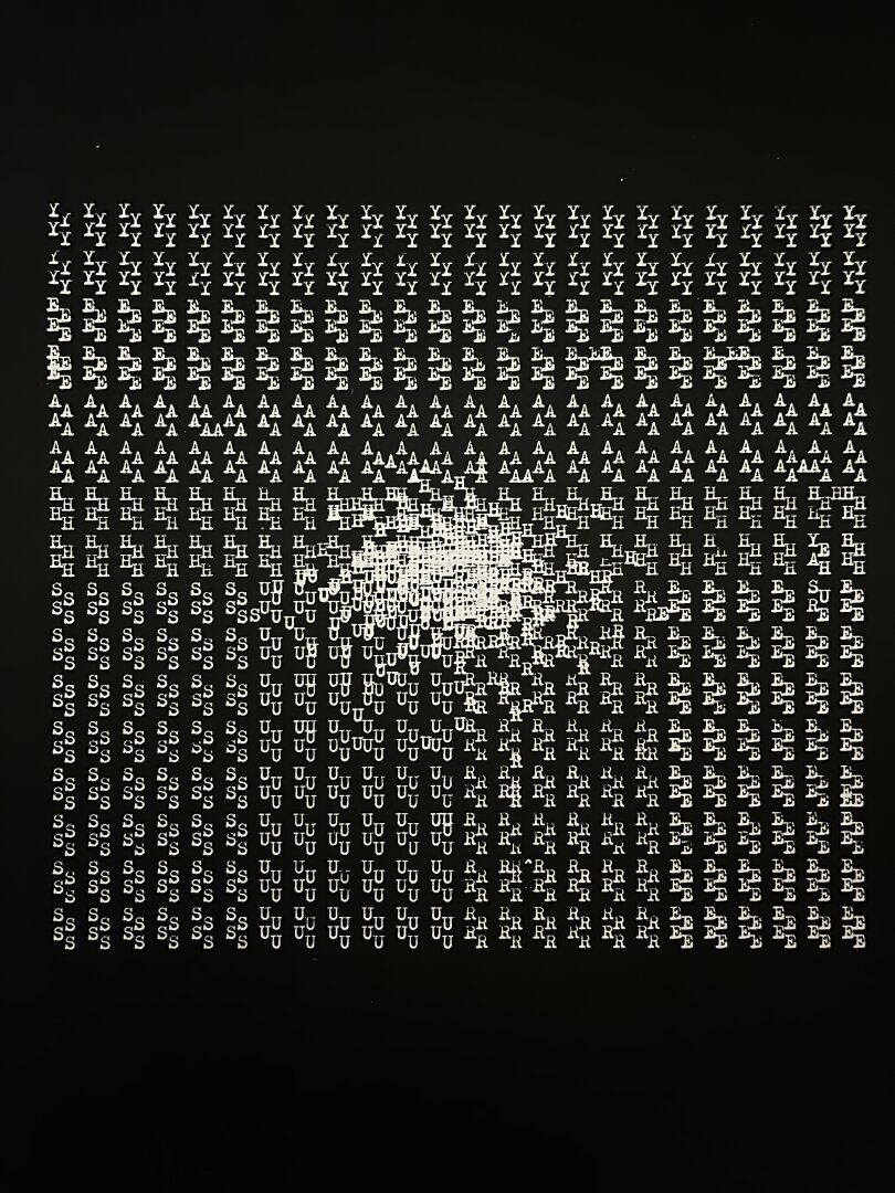 An image with white text on a black background, the text was produced on a typewriter and creates a square. The top half of the square says ‘yeah’ and the bottom half of the square says ‘sure’. in the middle of the square there is a kind of chaos as letters overlap. This effect seems to almost create a black hole, or in this case a white hole as the ink is white.