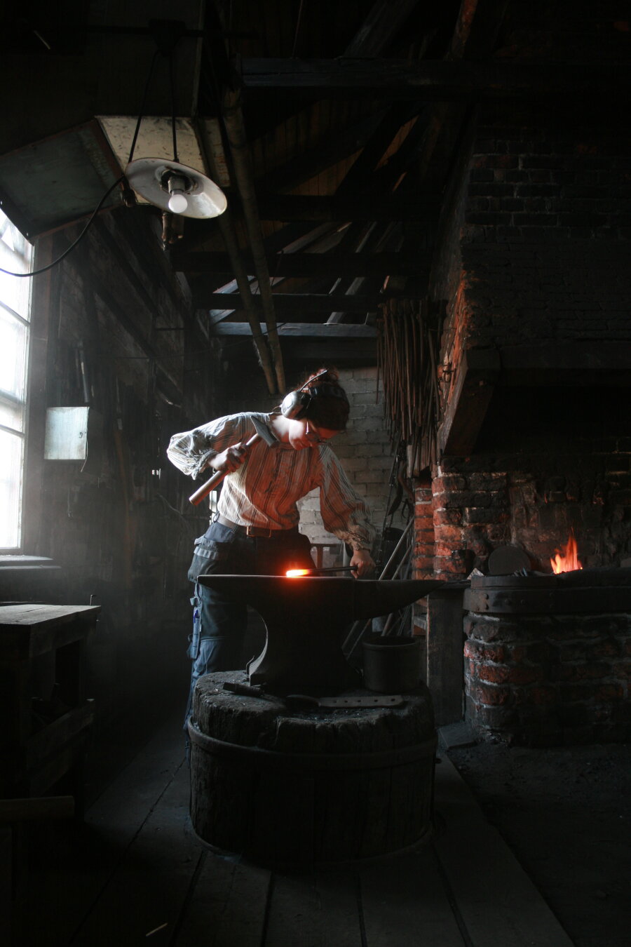 Photo of the blacksmith Linnea at her previous forge. Swinging a hammer