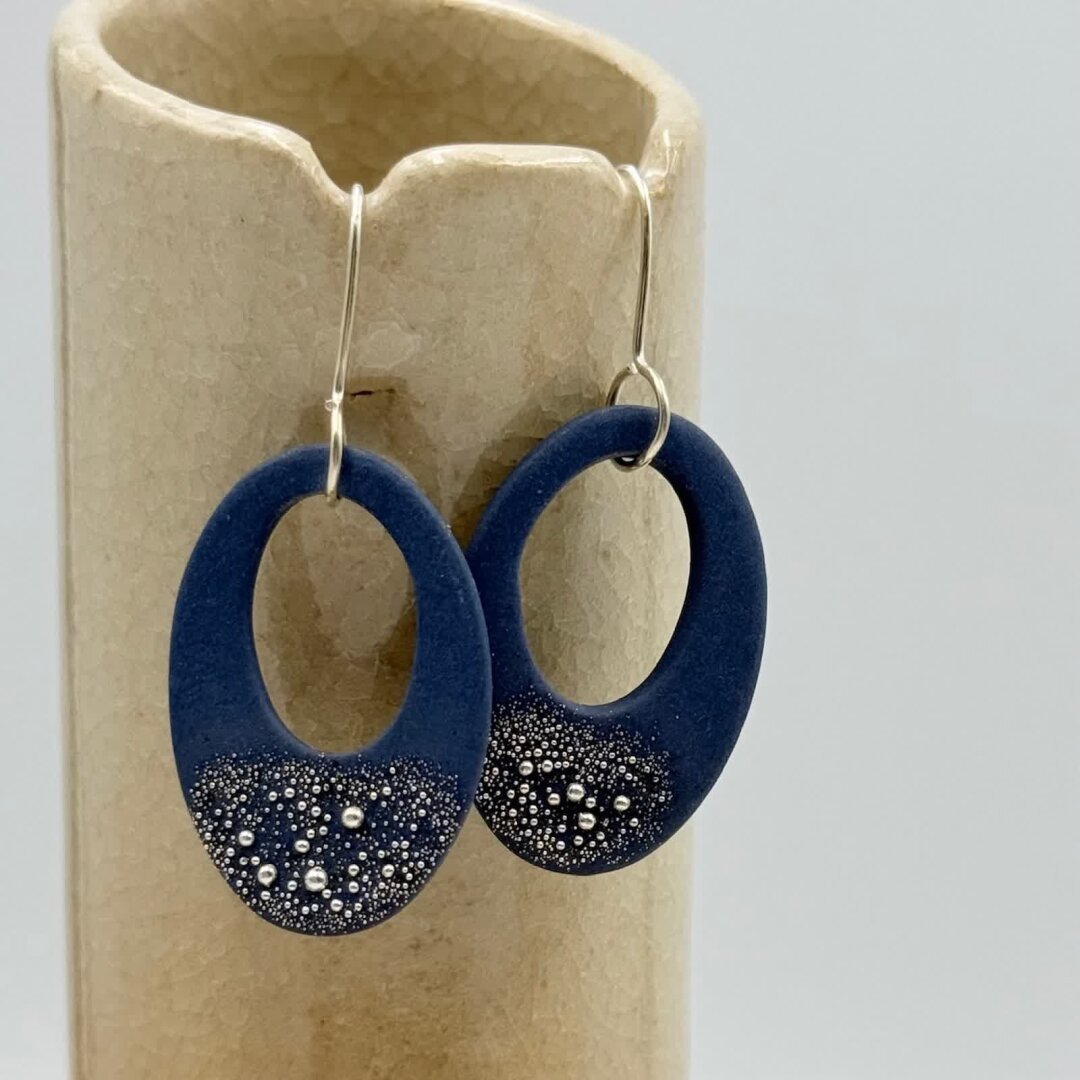 Boucles d’oreilles représentant un ovale plat percé d'un ovale excentré. 
A la base de la boucle, des petites billes d'argent rappellent le ciel étoilé.
La tige est en argent 925 réalisée artisanalement à l'atelier.