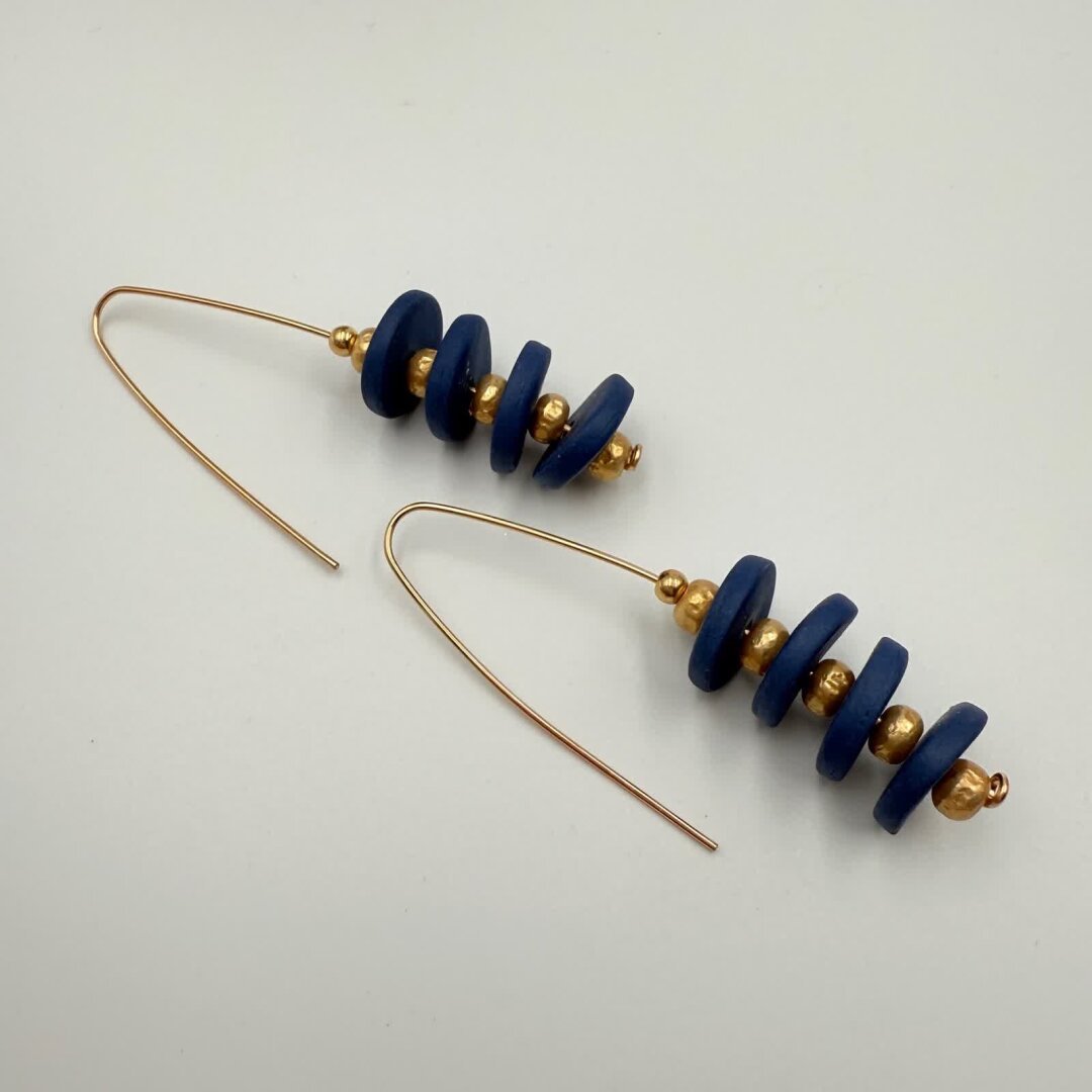 Boucles d’oreilles présentant un empilement de 4 disques en porcelaine bleue teintée dans la masse séparée par des perles dorées.
La tige est en Gold Filled réalisée artisanalement à l'atelier.