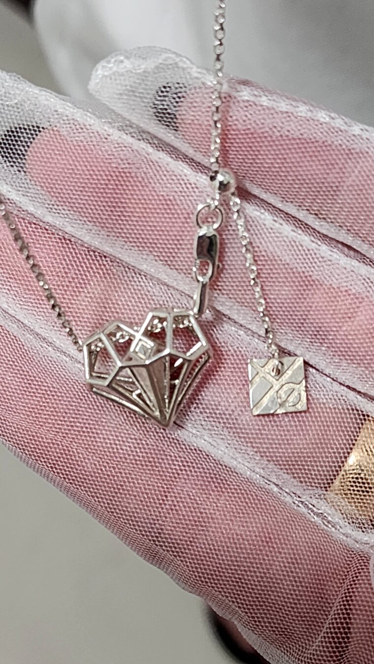 A hand in a white mesh glove holds a silver necklace with a geometric heart pendant on a fine chain. 
~
Een hand in een witte netten handschoen houdt een zilveren ketting met een geometrisch hartvormig hangertje aan een fijn kettinkje vast.
~
Une main gantée de résille blanche tient un collier en argent avec un pendentif en forme de cœur géométrique sur une fine chaîne.