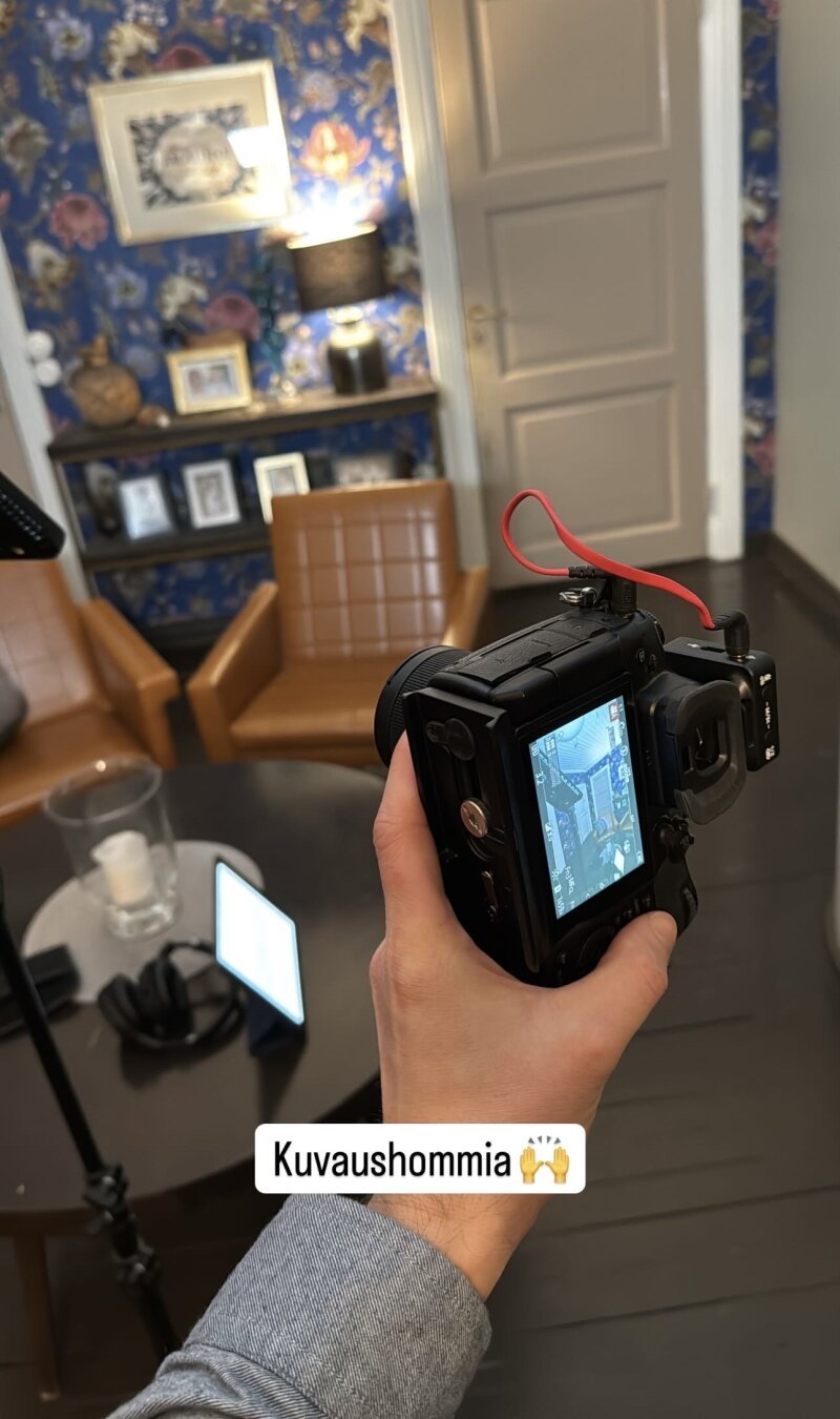 Kuvaajan kädessä järjestelmäkamera. Retro-henkisesti sisustettu huone taustalla.